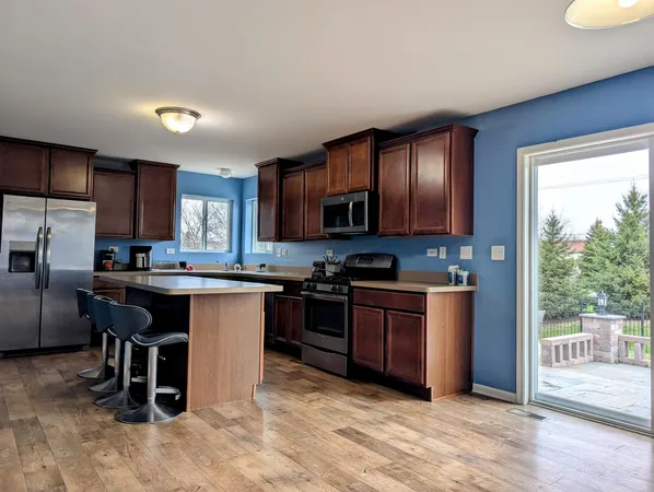 a kitchen with stainless steel appliances granite countertop a refrigerator a sink dishwasher a stove a dining table and chairs with wooden floor