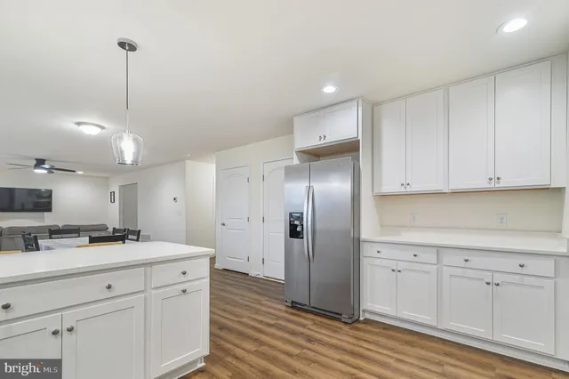 a kitchen with stainless steel appliances kitchen island granite countertop a refrigerator a sink dishwasher and white cabinets with wooden floor