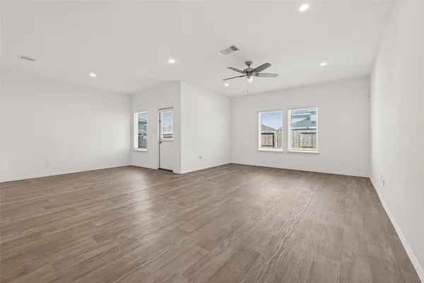 an empty room with wooden floor ceiling fan and windows