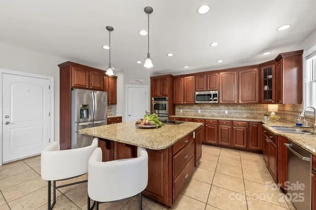 a kitchen with stainless steel appliances granite countertop a refrigerator a stove a sink a dining table and chairs