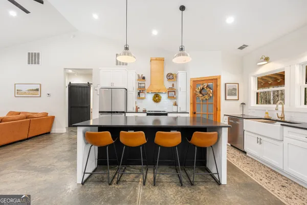 a kitchen with stainless steel appliances granite countertop a refrigerator a sink a stove and a dining table with wooden floor