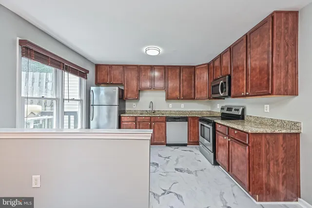 a kitchen with stainless steel appliances granite countertop a refrigerator a sink dishwasher a stove top oven a large countertops with wooden cabinets and floor