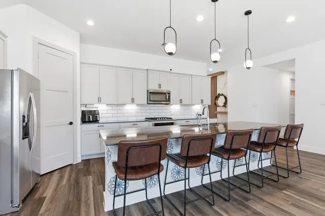 a kitchen with stainless steel appliances kitchen island granite countertop a dining table chairs sink and cabinets