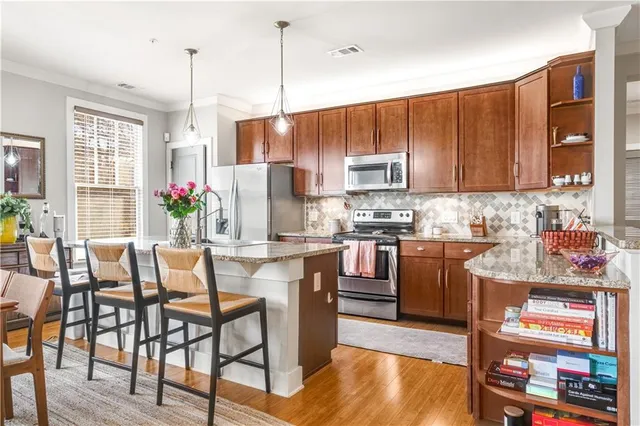 a kitchen with stainless steel appliances granite countertop a refrigerator a stove top oven a sink dishwasher and a dining table with wooden floor