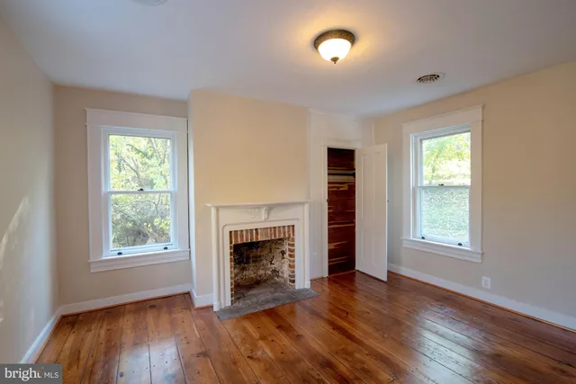 an empty room with windows a fireplace and wooden floor
