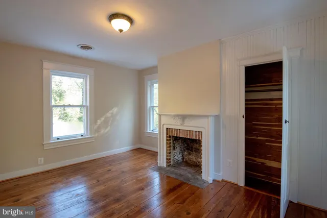 an empty room with wooden floor fireplace and windows