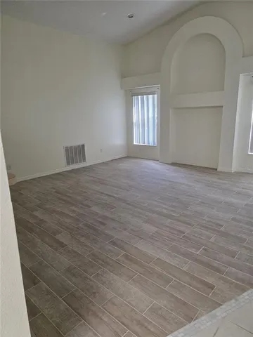 a view of an empty room with wooden floor and window