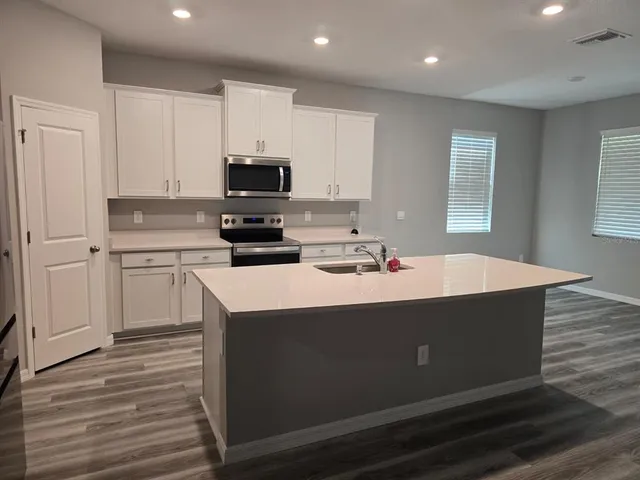 a kitchen with kitchen island a sink dishwasher a stove and white cabinets with wooden floor