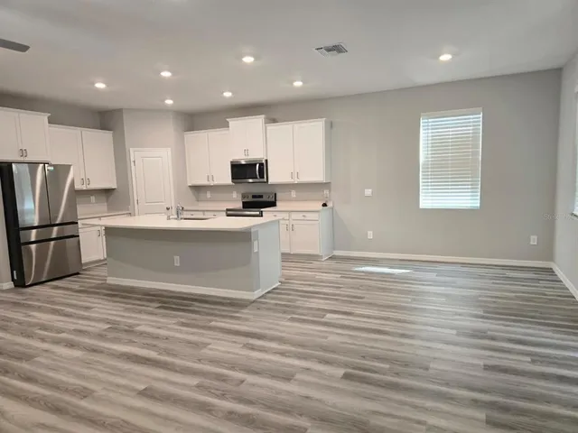 a large kitchen with kitchen island a sink dishwasher a stove a refrigerator and white cabinets with wooden floor