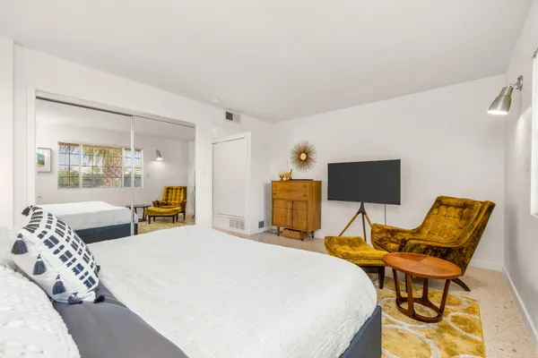 a bedroom with a bed a chair and the dresser next to a window