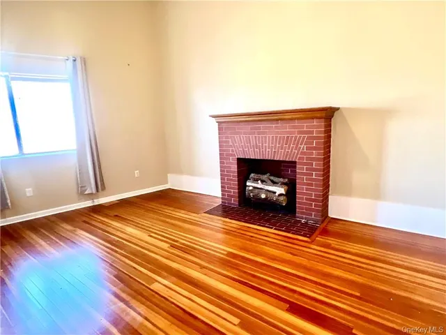 a view of an empty room with wooden floor fireplace and a window