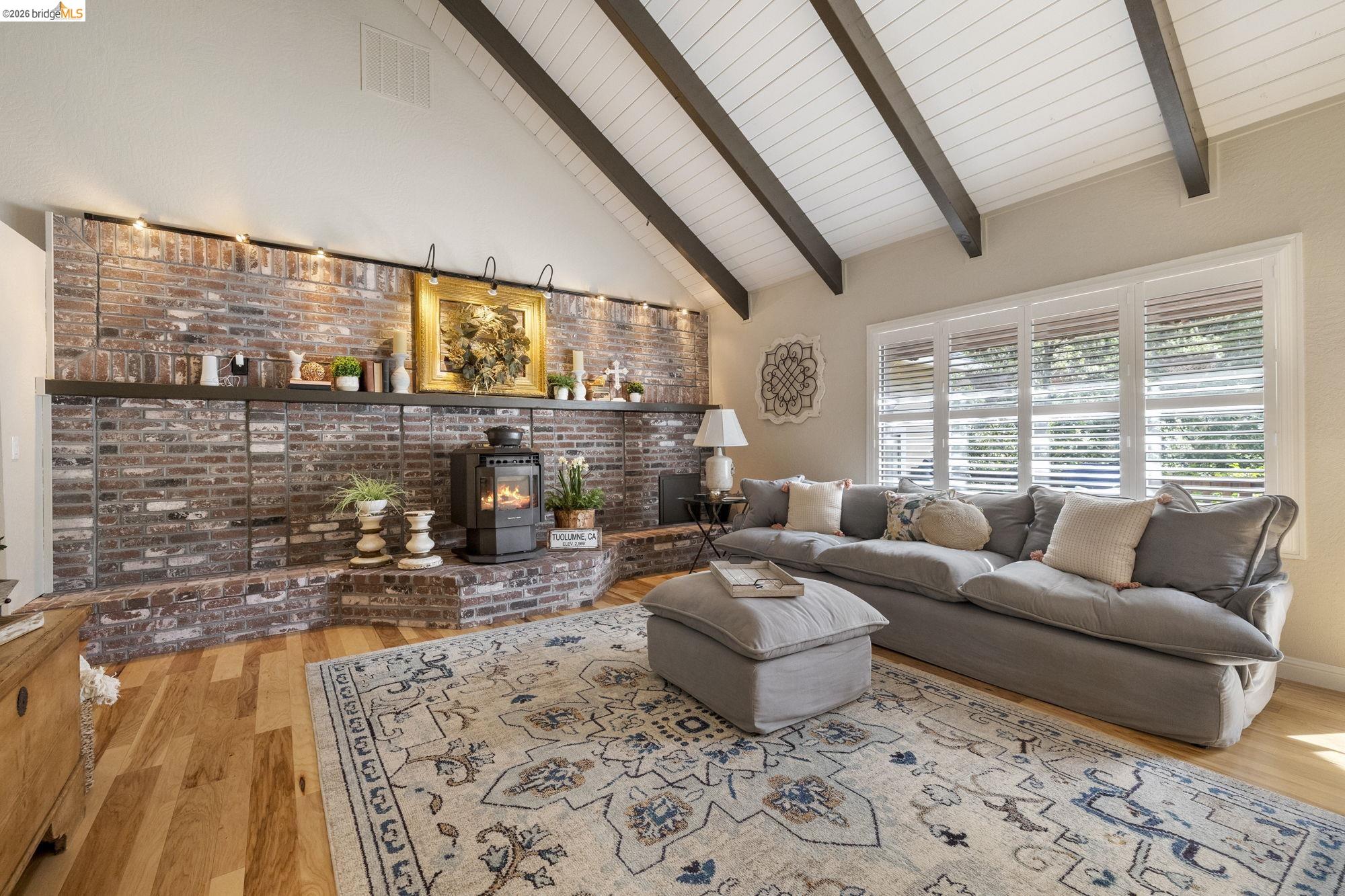 20581 Gerber Road Tuolumne, CA 95379 - Photo 18 of 60 Living area with high vaulted ceiling, a wood stove, beam ceiling, light wood-style flooring, and brick wall