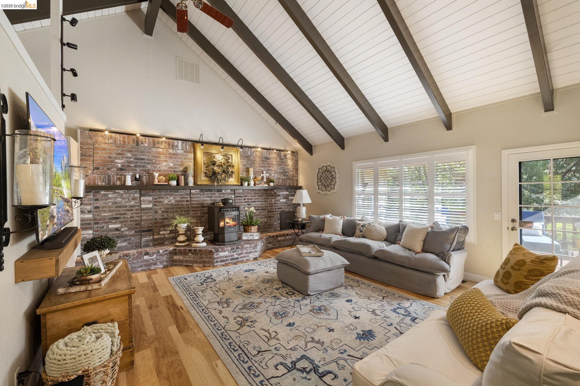 20581 Gerber Road Tuolumne, CA 95379 - Photo 19 of 60 Living room with high vaulted ceiling, beamed ceiling, a wood stove, and light wood-type flooring