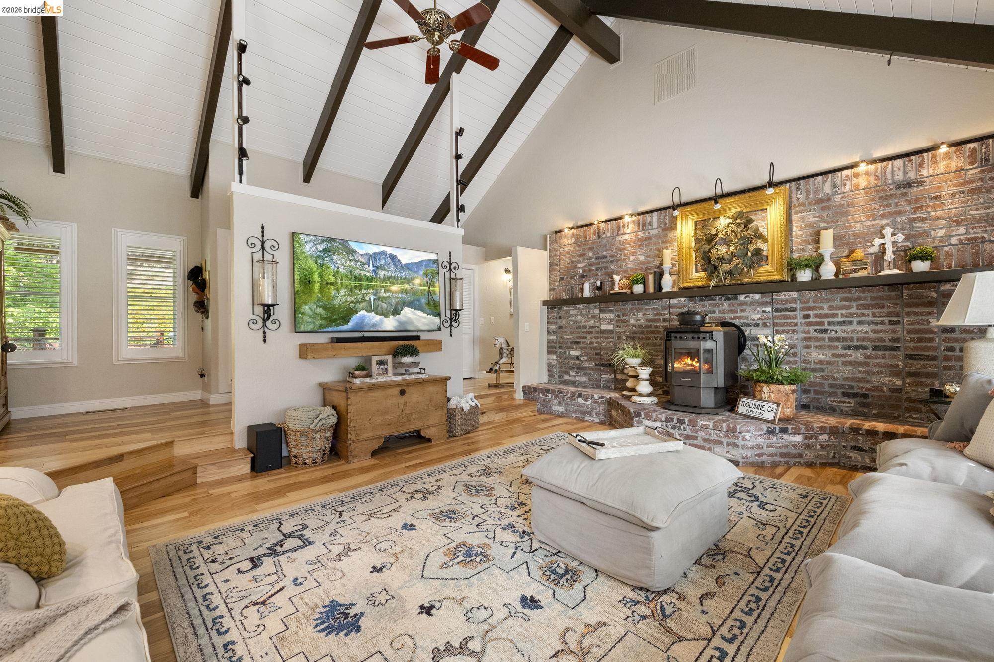 20581 Gerber Road Tuolumne, CA 95379 - Photo 20 of 60 Living room featuring high vaulted ceiling, beam ceiling, wood finished floors, a wood stove, and a ceiling fan