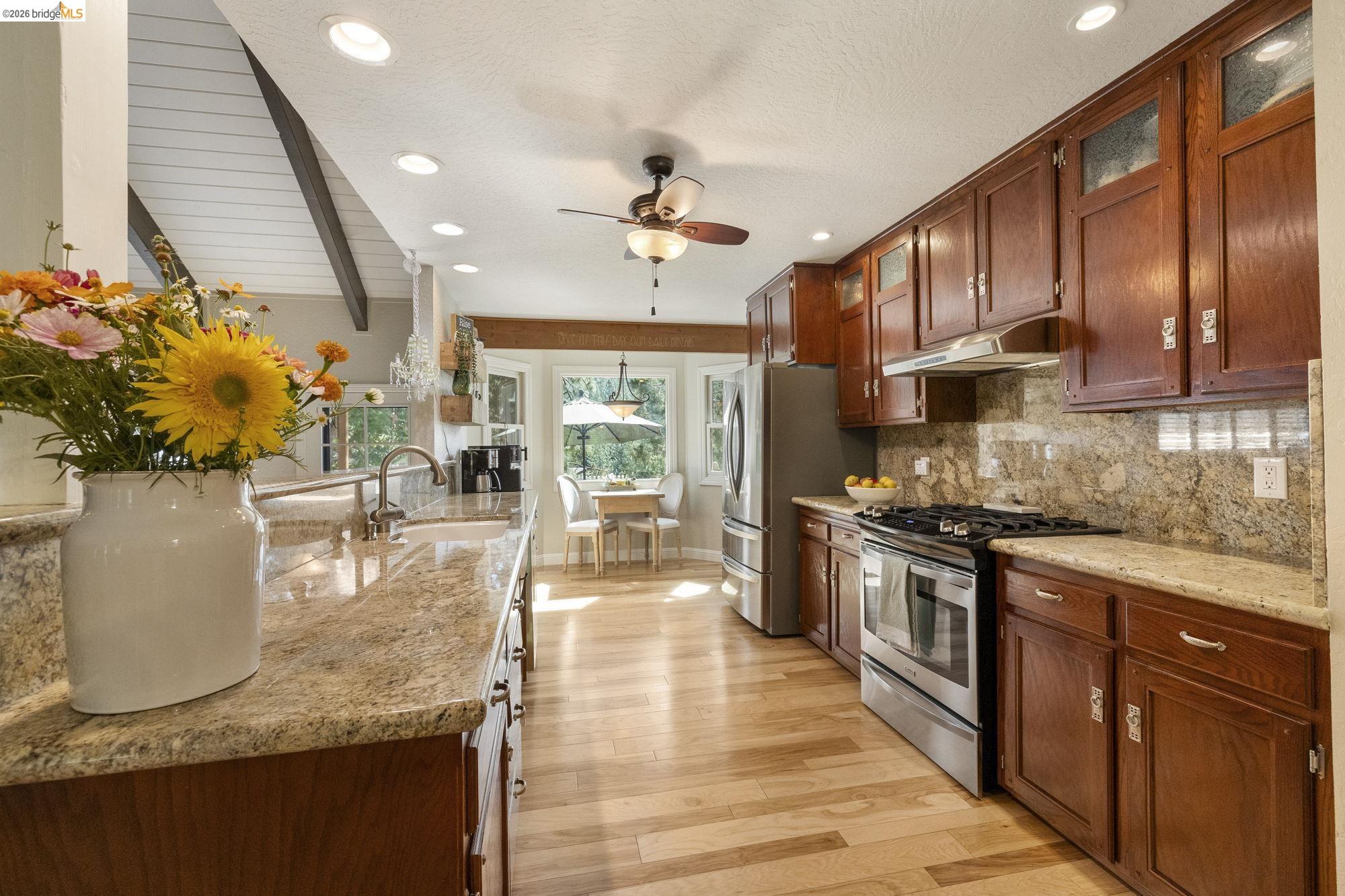 20581 Gerber Road Tuolumne, CA 95379 - Photo 10 of 60 Kitchen featuring appliances with stainless steel finishes, tasteful backsplash, light stone countertops, glass insert cabinets, and light wood finished floors