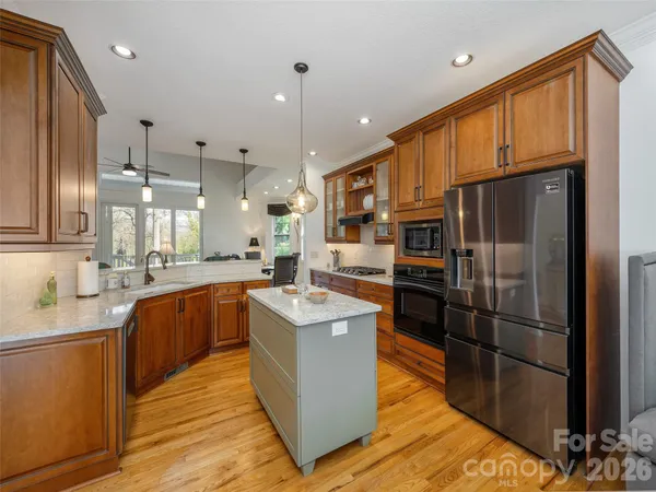 a large kitchen with stainless steel appliances granite countertop a refrigerator a sink dishwasher a oven and a dining table with wooden floor