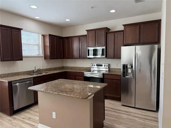 a kitchen with kitchen island granite countertop wooden cabinets a refrigerator and a stove top oven