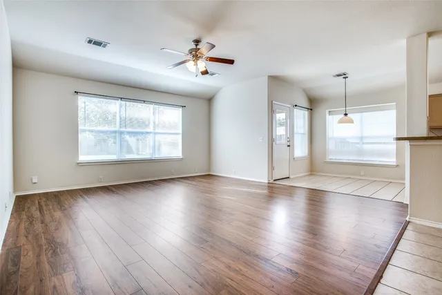 an empty room with wooden floor chandelier and windows