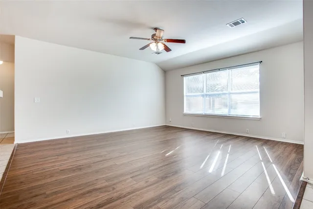 an empty room with wooden floor ceiling fan and windows