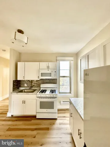 a large white kitchen with stainless steel appliances granite countertop a stove and a sink