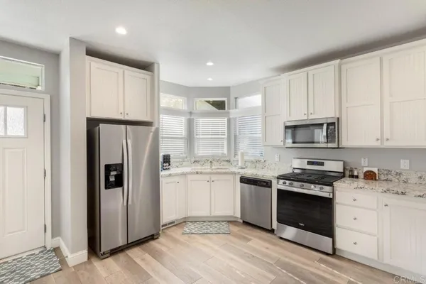 a kitchen with stainless steel appliances granite countertop a stove top oven a refrigerator a sink and dishwasher with white cabinets