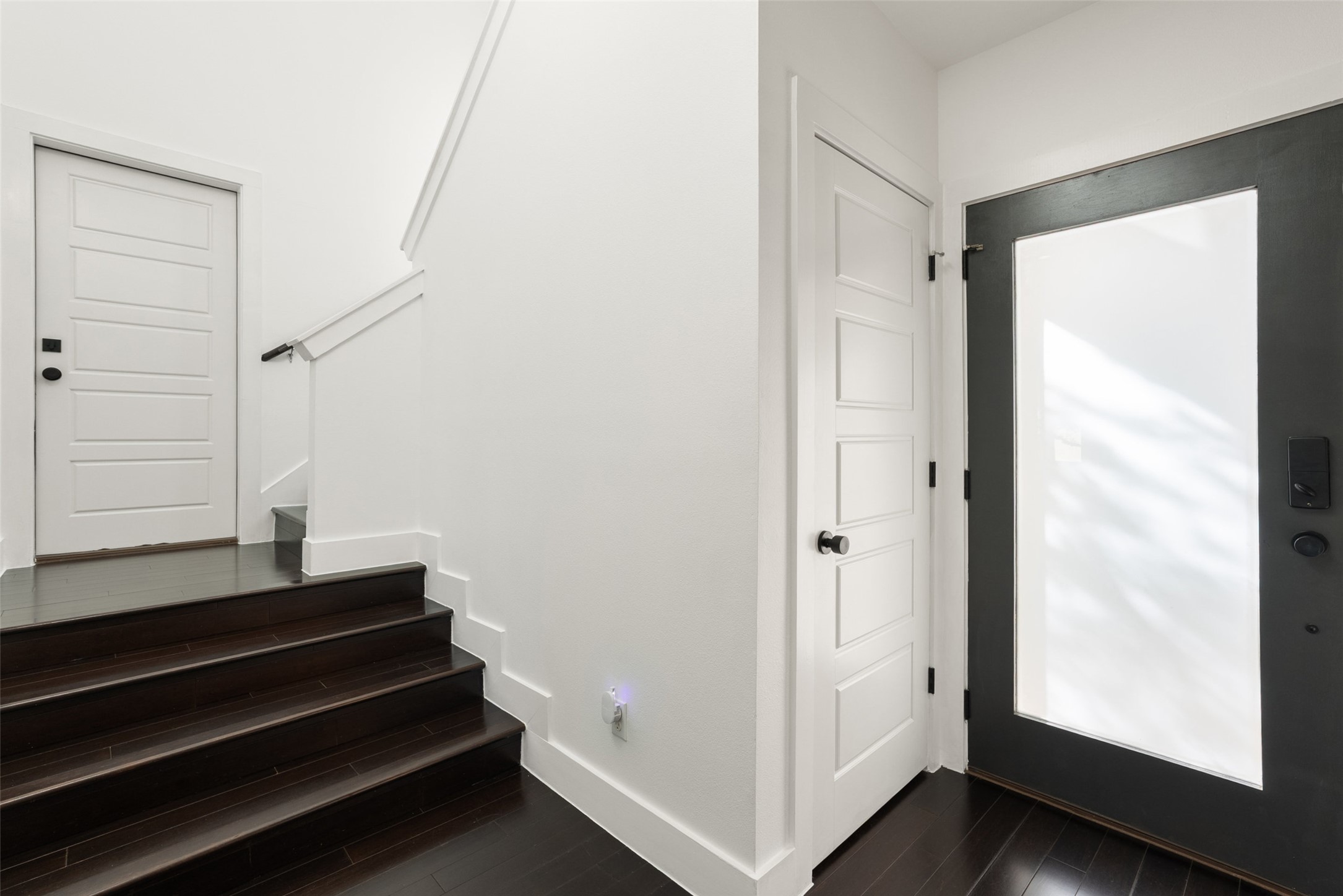 1303 Azie Morton Road, Unit 6 Austin, TX 78704 - Photo 31 of 40 This modern entryway features dark wood floors and stair treads dramatically contrasting with crisp white walls and trim. A large, dark-framed glass entry door maximizes light, and the dark staircase immediately establishes the home's contemporary, multi-level design.