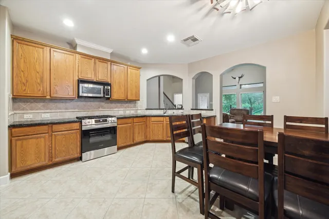 a kitchen with stainless steel appliances granite countertop wooden cabinets a stove a sink a dining table and chairs