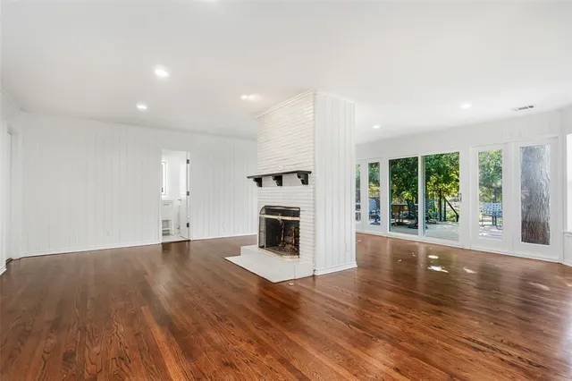 an empty room with wooden floor fireplace and windows