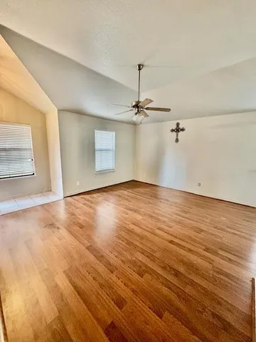 an empty room with wooden floor fan and windows