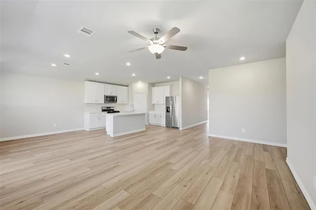 a view of an empty room with wooden floor and a kitchen