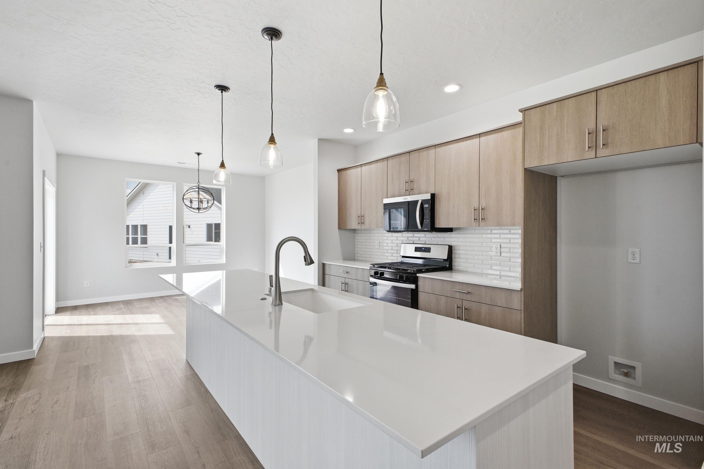 5293 South Memory Avenue Meridian, ID 83642 - Photo 4 of 24 Kitchen with stainless steel appliances, a kitchen island with sink, dark wood-style flooring, backsplash, and light stone counters
