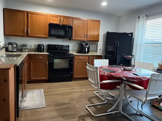 a kitchen with stainless steel appliances granite countertop a stove top oven a refrigerator a sink and dishwasher with wooden floor