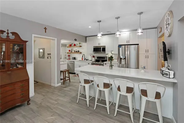 a kitchen with stainless steel appliances kitchen island granite countertop a dining table chairs and a refrigerator