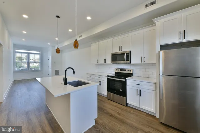 a kitchen with stainless steel appliances granite countertop a sink dishwasher a refrigerator and a stove with wooden floor