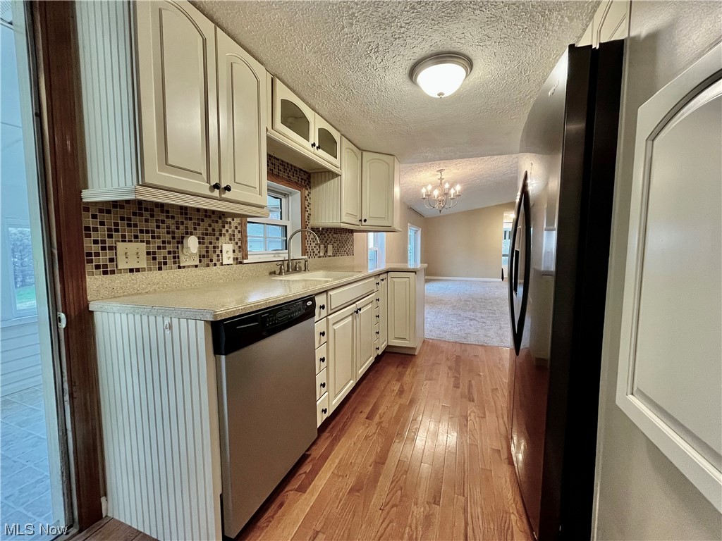 4214 School House Road Little Hocking, OH 45742 - Photo 18 of 29 Kitchen with light hardwood / wood-style floors, stainless steel dishwasher, sink, backsplash, and a notable chandelier