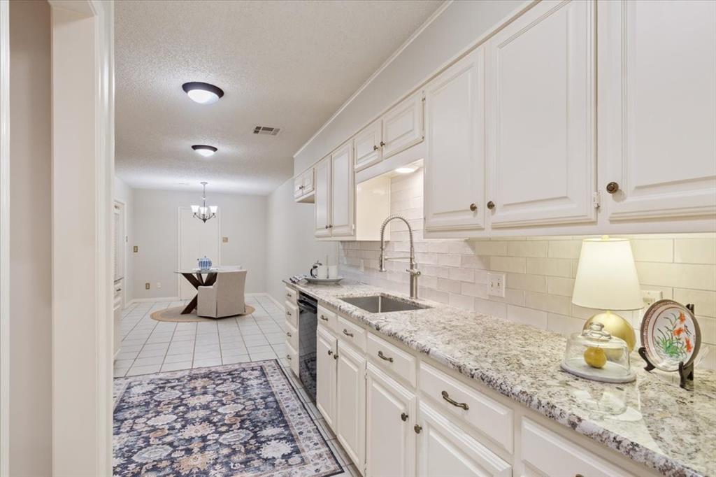 4108 Old Mill Road Waco, TX 76710 - Photo 16 of 39 Elegant galley kitchen featuring crisp white cabinetry with hardware accents, granite countertops, a tile backsplash, and a pull-down faucet over the sink