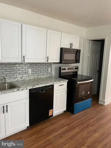 a kitchen with granite countertop a refrigerator a stove a sink and white cabinets with wooden floor