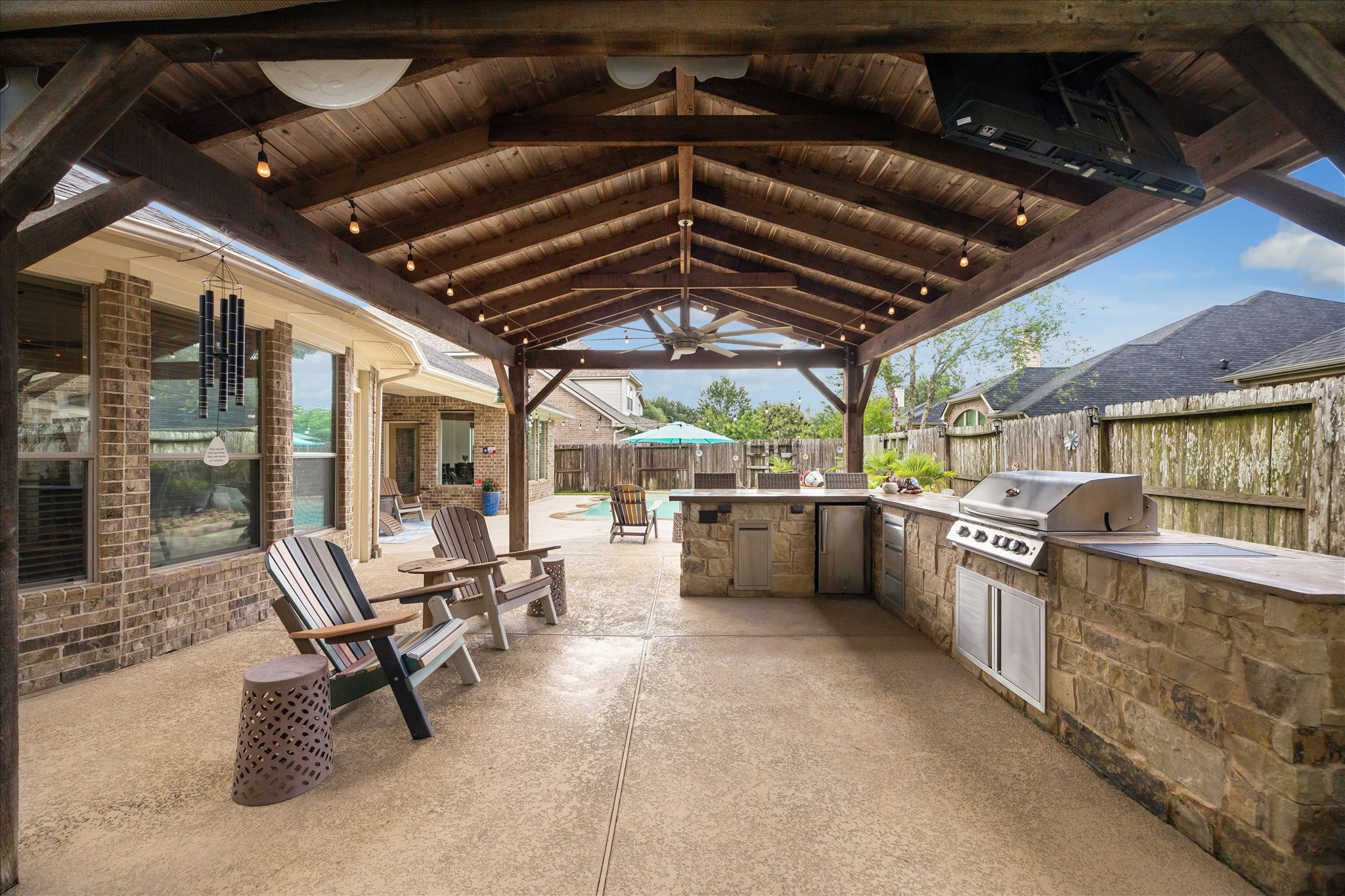 28211 Rippling Brook Lane Fulshear, TX 77441 - Photo 29 of 45 OUTDOOR KITCHEN: Impressive covered outdoor kitchen features concrete countertops, stainless steel grill, refrigerator, added storage, built-in speakers, and a striking wood-beam structure with a statement 9-blade fan.