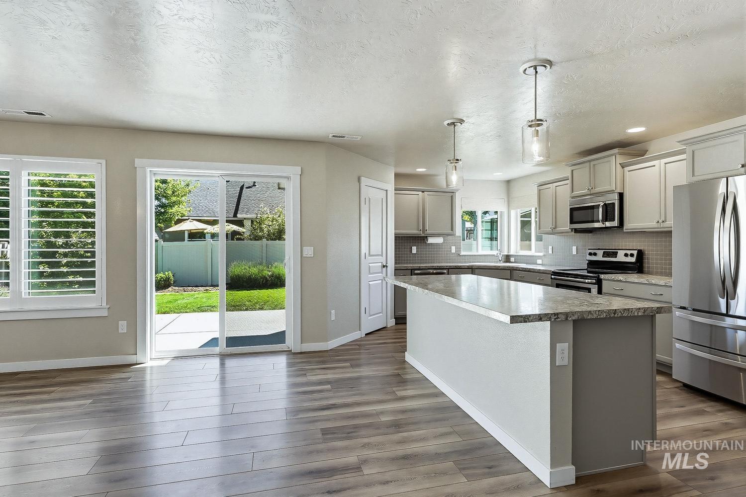 846 North Hidden View Way Star, ID 83669 - Photo 8 of 49 Open concept kitchen featuring a large island with a stone-finish countertop, stainless steel appliances, pendant lighting, and wood-finish flooring