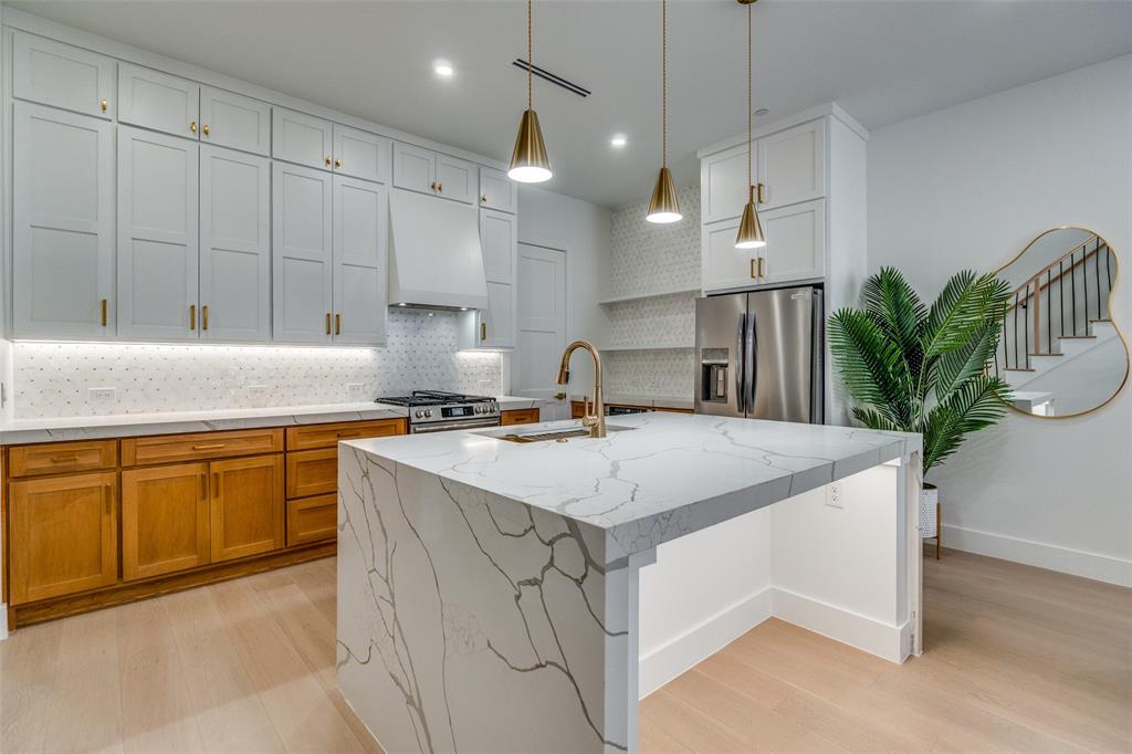 708 West 10th Street, Unit 101 Dallas, TX 75208 - Photo 2 of 10 Not Actual_Model Kitchen with light stone counters, decorative backsplash, a center island with sink, appliances with stainless steel finishes, and light wood-style floors