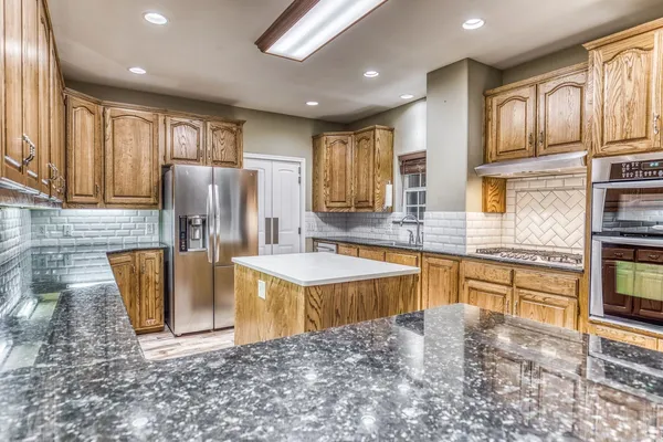 a large kitchen with kitchen island granite countertop a sink refrigerator and cabinets