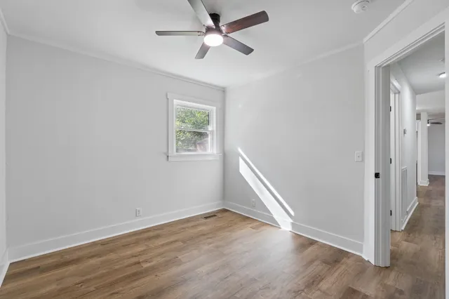 an empty room with wooden floor ceiling fan and windows