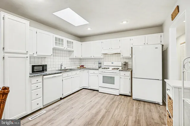 a kitchen with wooden floors white appliances white cabinets and a sink