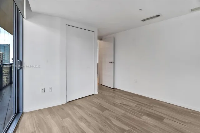 an empty room with wooden floor closet and windows