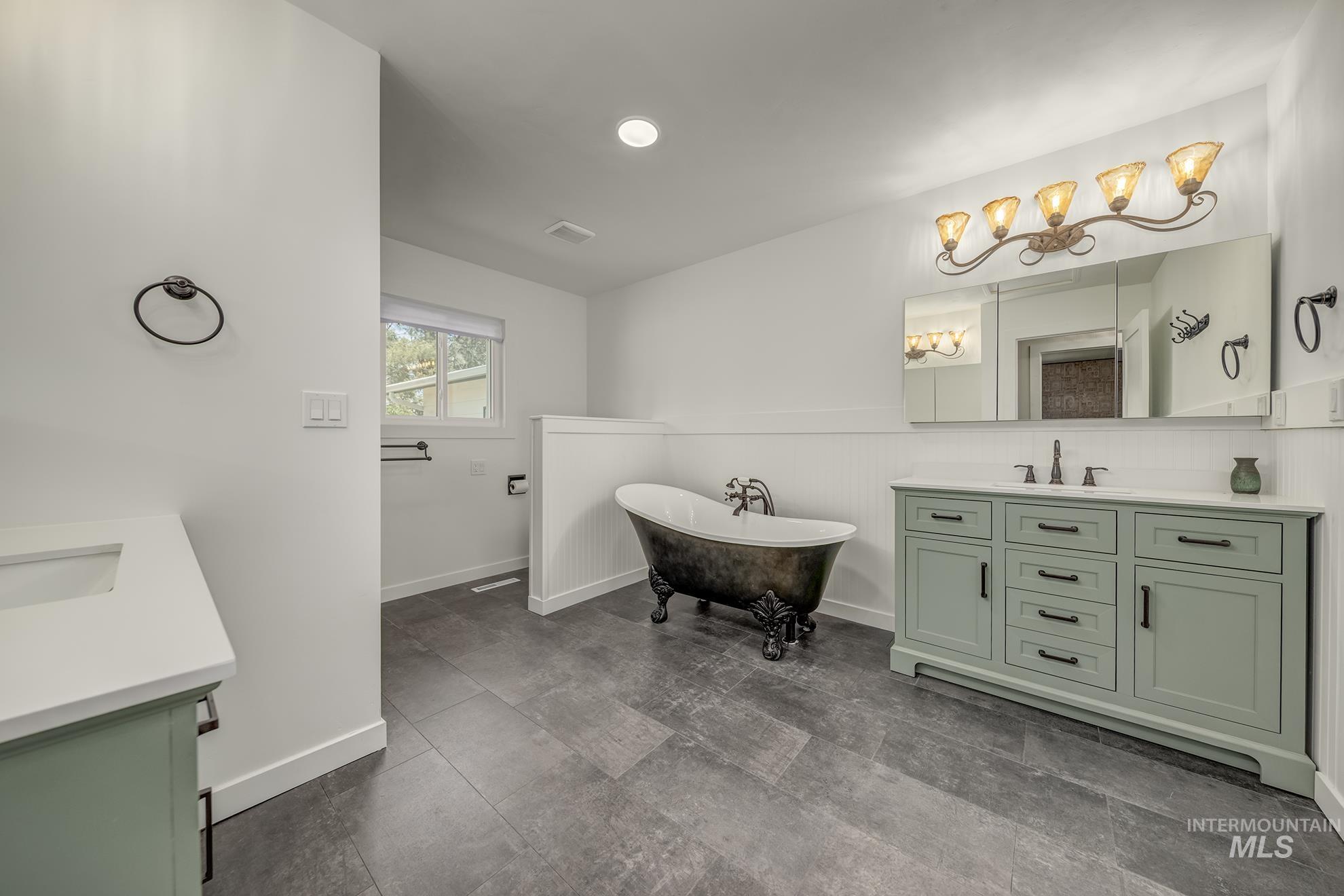 748 Pringle Road Weiser, ID 83672 - Photo 15 of 47 Spacious bathroom featuring a freestanding clawfoot tub, dual sage green vanities with integrated sinks and white countertops, dark floor tiling, and a large mirrored medicine cabinet with decorative lighting