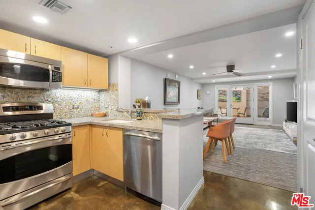 a kitchen with stainless steel appliances granite countertop a stove top oven a sink dishwasher a dining table and chairs with wooden floor