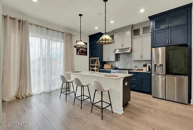 a kitchen with stainless steel appliances granite countertop a refrigerator a sink dishwasher a stove and white countertops with wooden floor