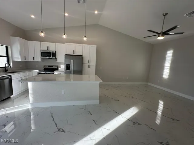 a large kitchen with stainless steel appliances a large counter top a stove a sink a refrigerator and a window