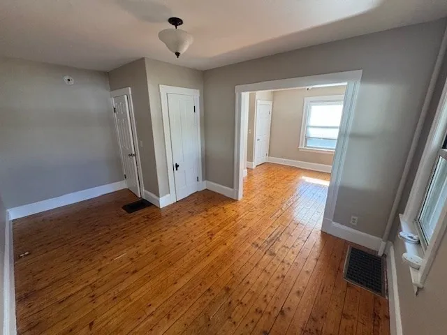 a view of an empty room with wooden floor and a window