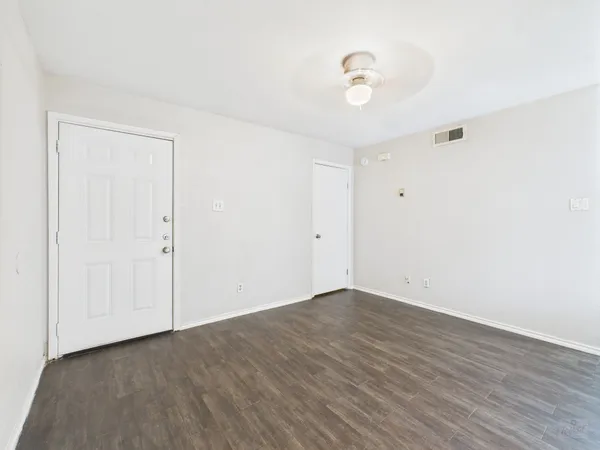 a view of an empty room with wooden floor and a ceiling fan